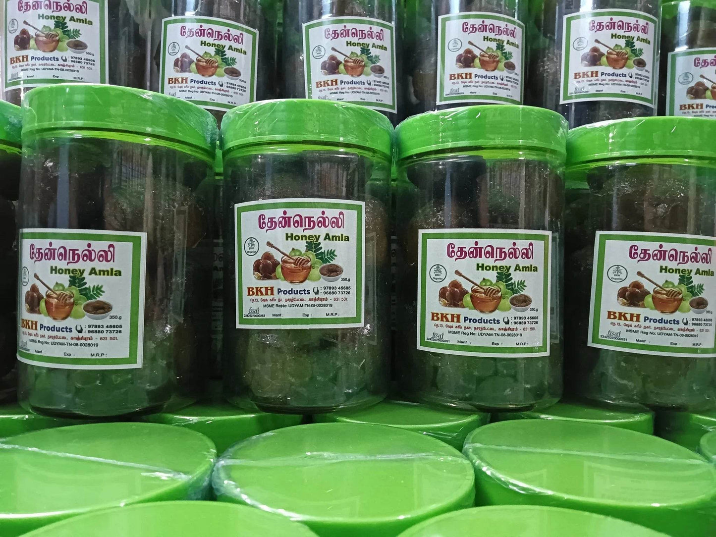 Multiple jars of BKH Products honey with green lids on a green surface.