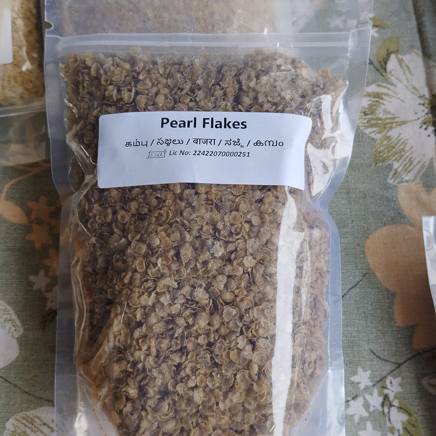 Packaged pearl flakes with a label on a floral-patterned surface, BKH Kambu Flakes, BKH Pearl millet Flakes