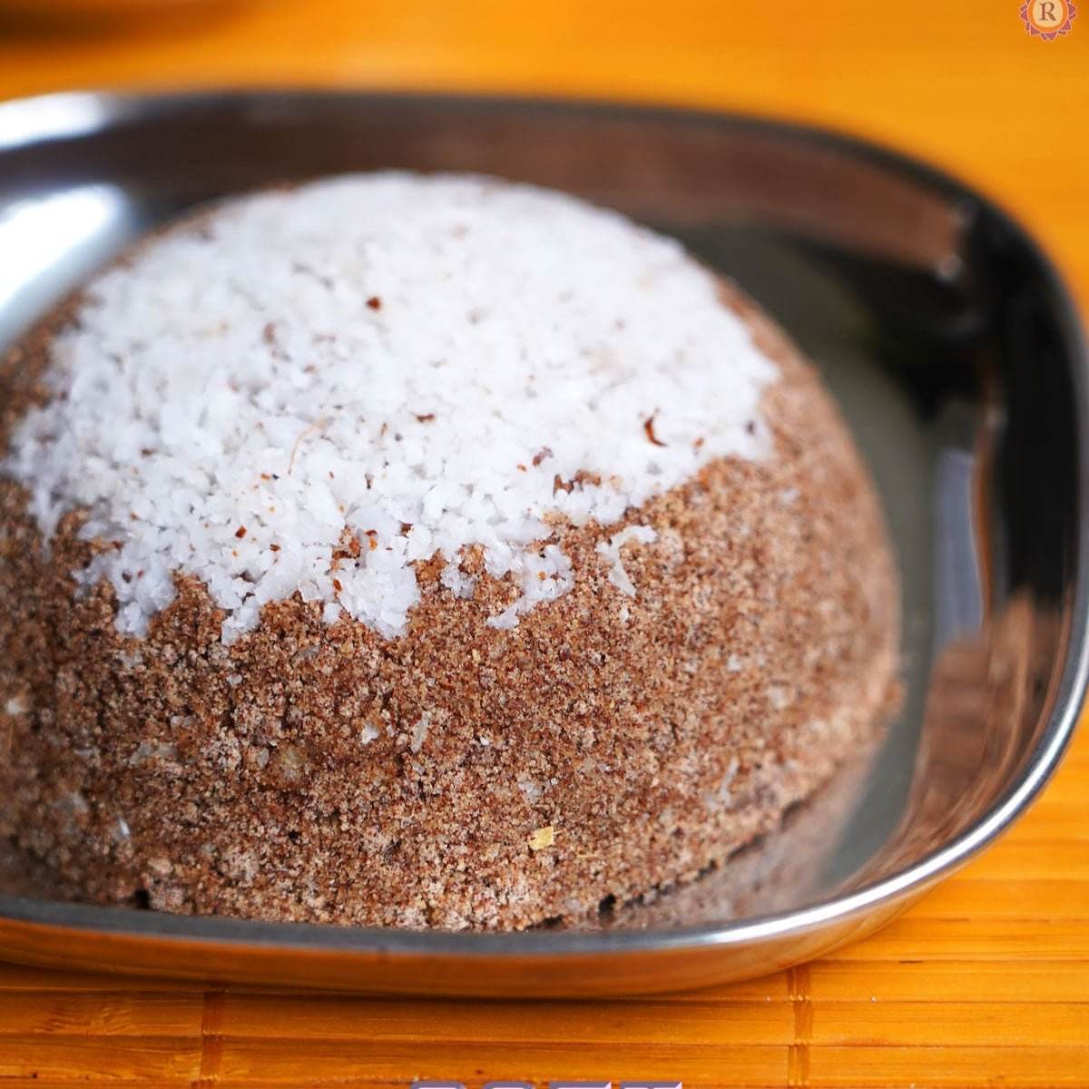 Round cake with white and brown toppings on a metal tray. Ragi Puttu Mavu 500g - BKH Organics