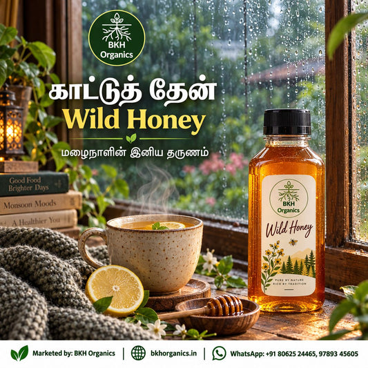 A bottle of BKH Organics Wild Honey is displayed on a windowsill next to a steaming cup of tea with lemon, a honey dipper, and a knit blanket, with raindrops on the window and promotional text in Tamil.