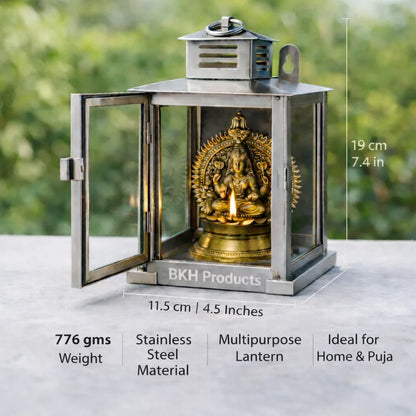 Stainless steel lantern with a gold statue inside, placed on a surface with a blurred green background. BKH