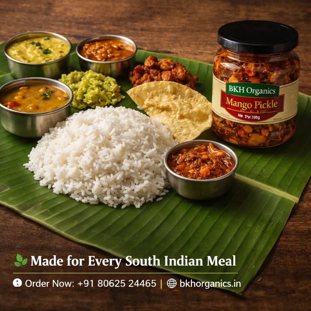 South Indian meal setup with rice, curries, and a jar of BKH Organics Mango Pickle on a wooden surface.
