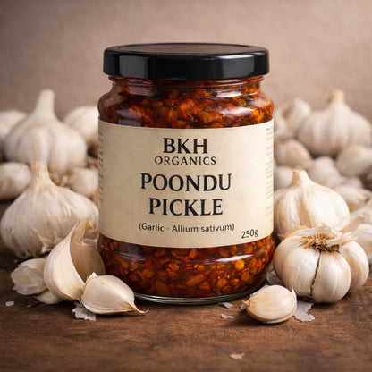 Jar of BKH Organics Poondu Pickle surrounded by garlic bulbs on a wooden surface.