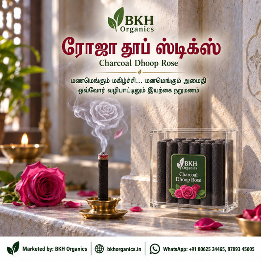 BKH Organics Charcoal Dhoop Rose advertisement showing a burning incense stick in a brass holder and a clear box of dark charcoal sticks with a rose label, set on a stone surface with a rose, petals, and lit diya in a real interior setting. BKH Organics Charcoal Dhoop Rose Sticks (தமிழ்: ரோஜா தூப் ஸ்டிக்ஸ், తెలుగు: గులాబీ ధూప్ స్టిక్స్, ಕನ್ನಡ: ಗುಲಾಬಿ ಧೂಪ್ ಕಡ್ಡಿಗಳು, മലയാളം: റോസ് ധൂപം / ധൂപ് സ്റ്റിക്കുകൾ, ತುಳು: ರೋಸ್ ಧೂಪ್ದ ಕಡ್ಡಿಕುಲು) lit on a brass holder with fragrant rose smoke and acrylic container box