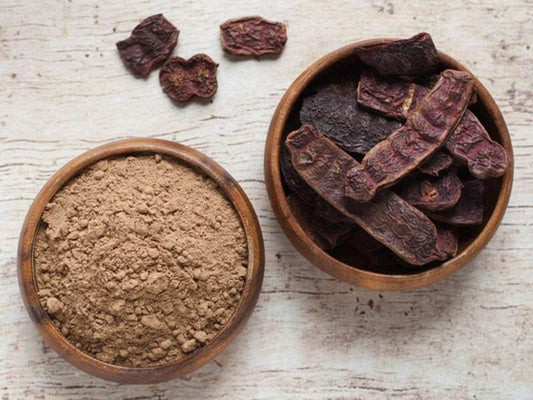 Two wooden bowls containing a brown powder and dried fruit on a light wooden surface.
