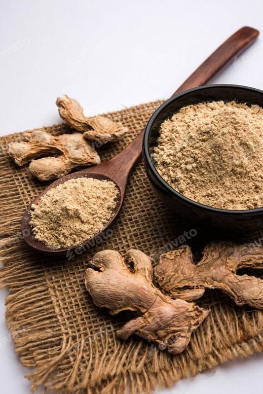 Ginger root and ground ginger powder on a burlap surface with a wooden. Sukku Herbal Powder 100g - BKH Organics spoon.