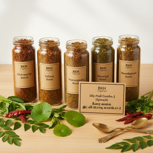 Five jars of spices with labels on a wooden surface, surrounded by herbs and a spoon.